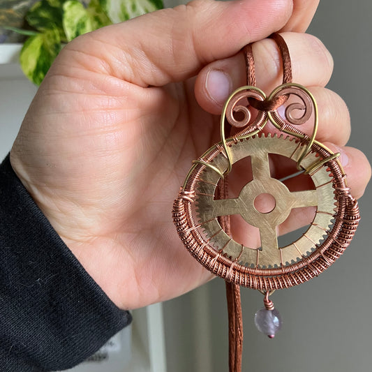 Hand holding a decorative keychain with intricate design and a purple gemstone.