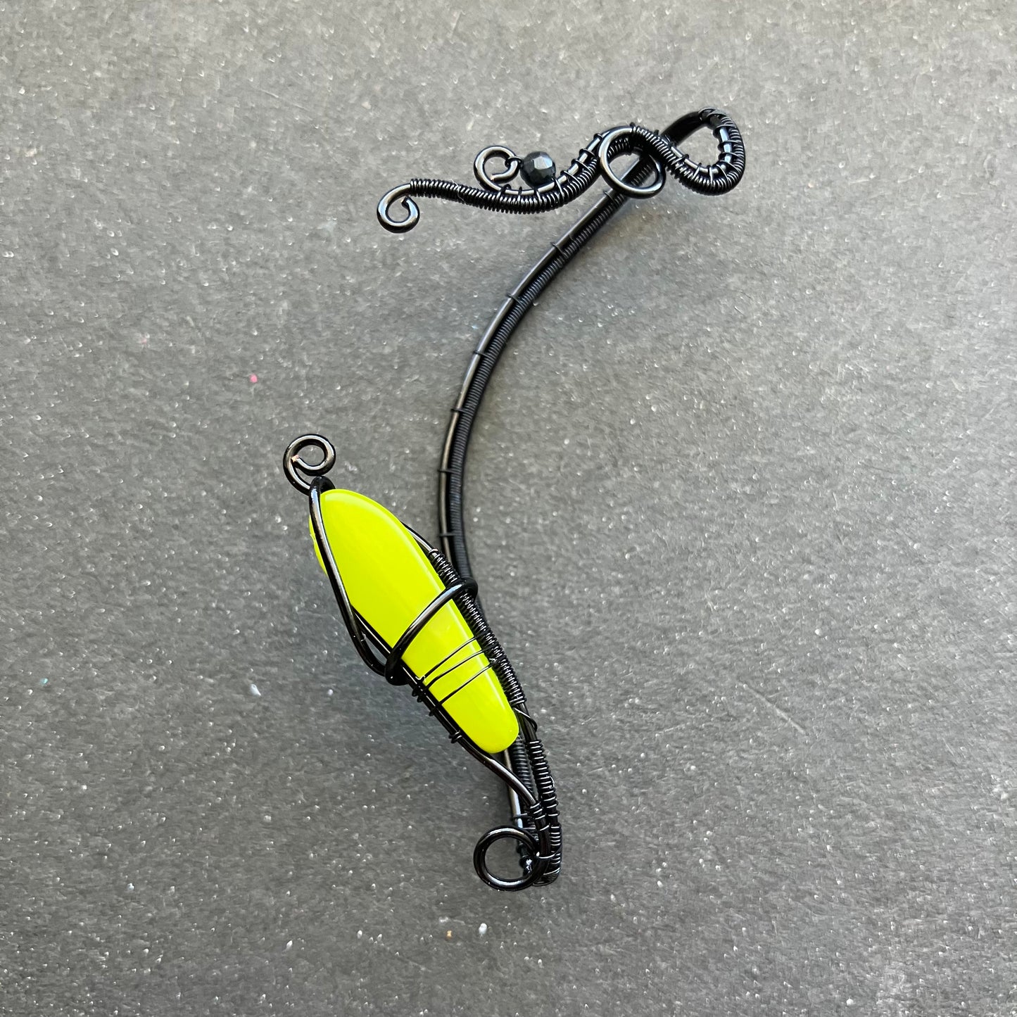 A black enameled copper wire ear wrap with a glass bead in lime green, designed to wrap around the ear.