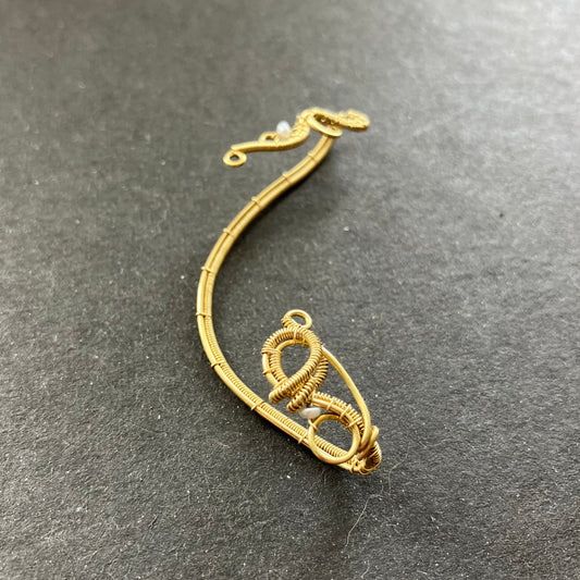 A gold-colored brass pearl ear wrap