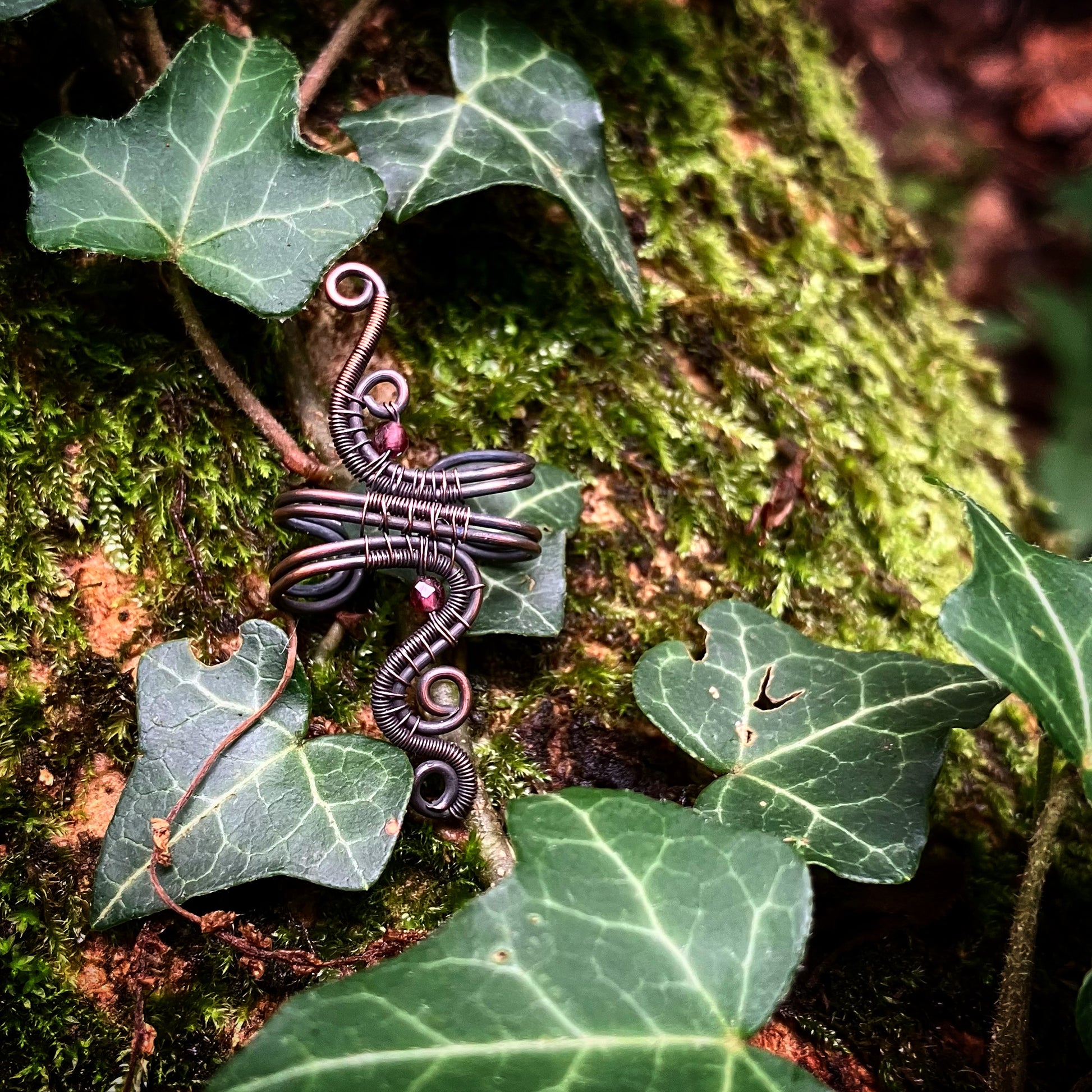 A copper garnet ear cuff placed on a mossy wooden surface with green leaves around it.