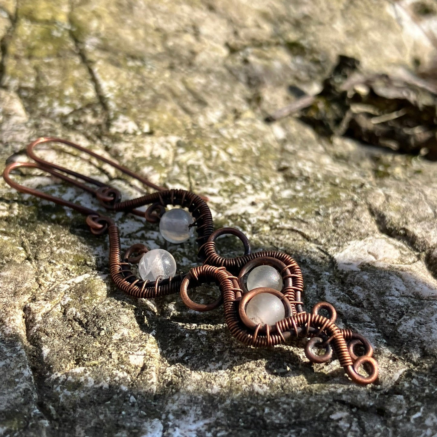Copper wire earrings with clear stones on a stone surface