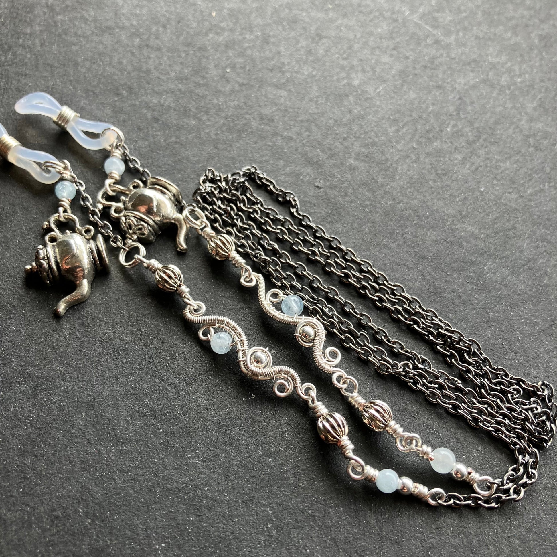 A silver-plated wire chain featuring aquamarine gemstone beads and metal teacup charms, with silicone rings.