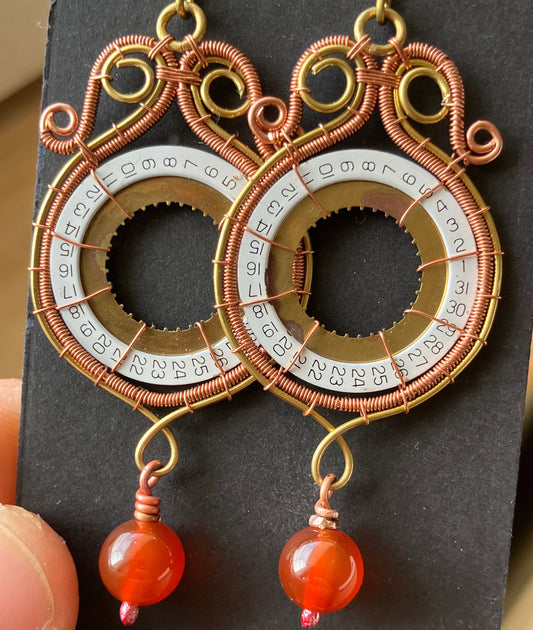 Decorative circular object with gold and copper elements and red beads on a dark background