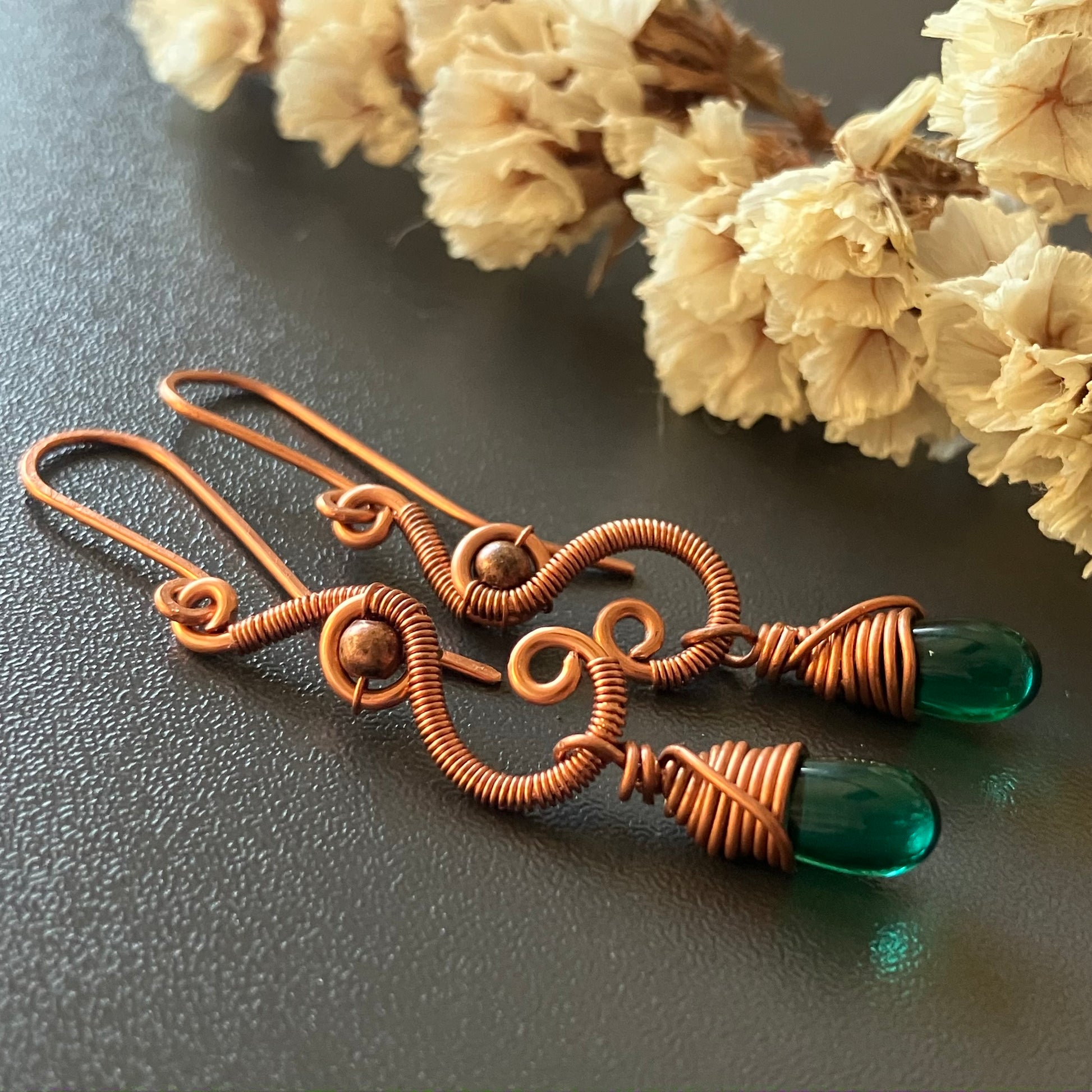 A pair of handmade copper wire drop earrings with green teardrop glass beads.