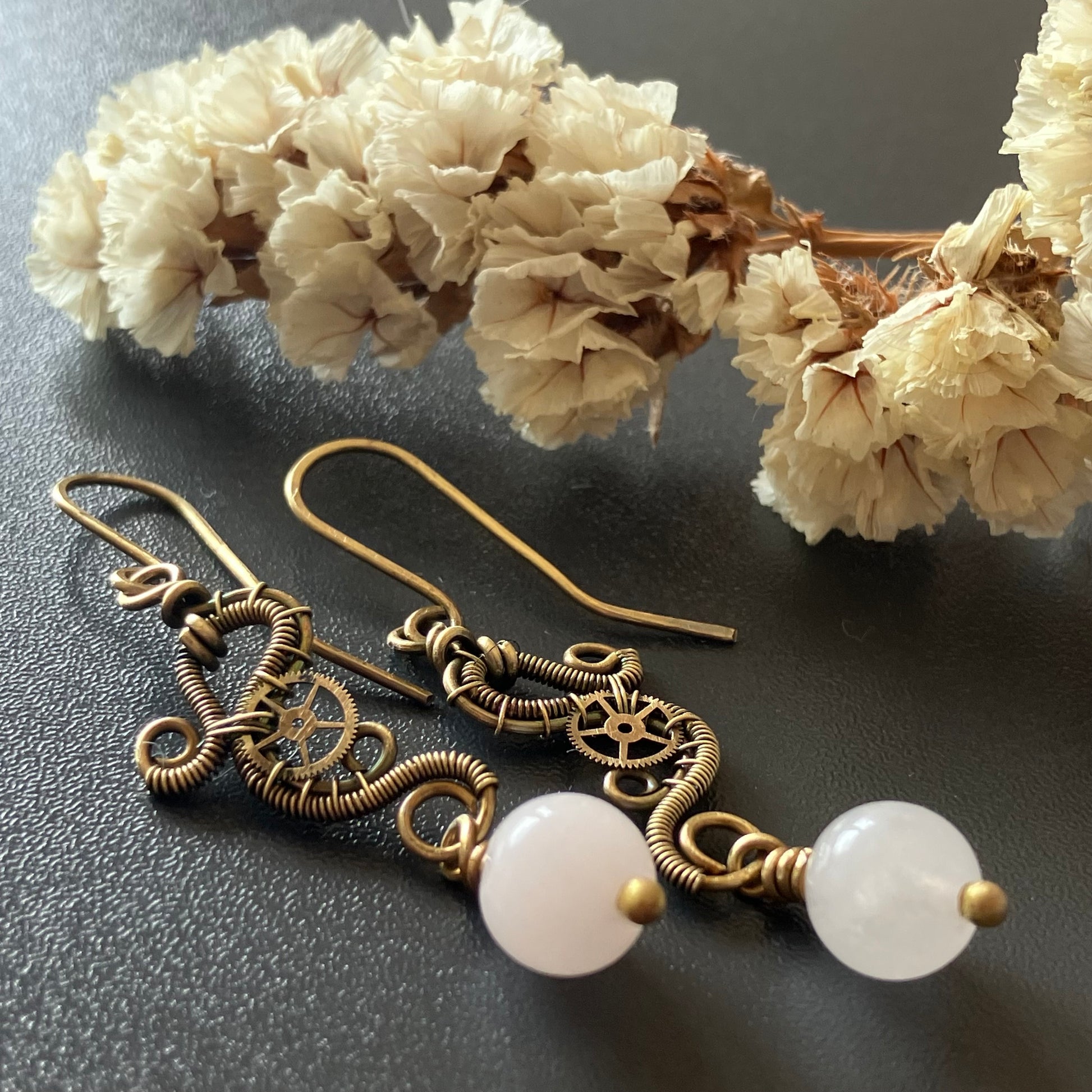 A pair of handmade steampunk dangle earrings with intricate gold-toned wirework and round rose quartz beads