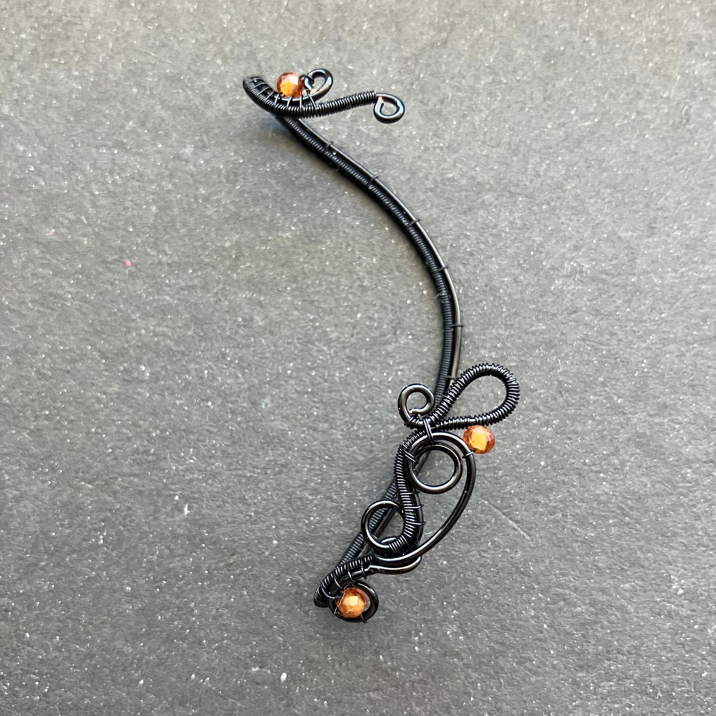 A black enameled copper wire ear wrap with hessonite stones attached to it.