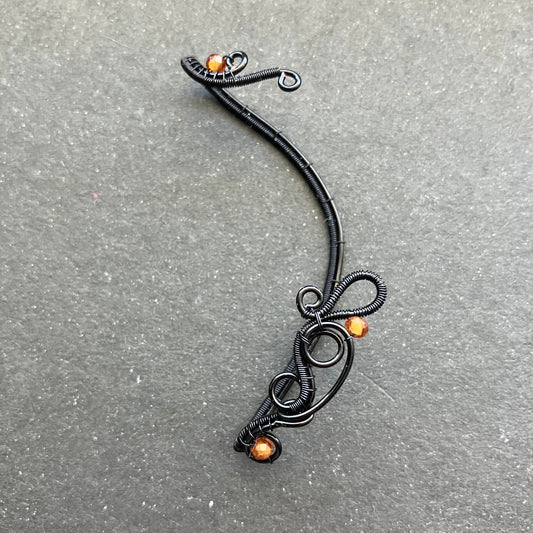 A black enameled copper wire ear wrap with hessonite stones attached to it.