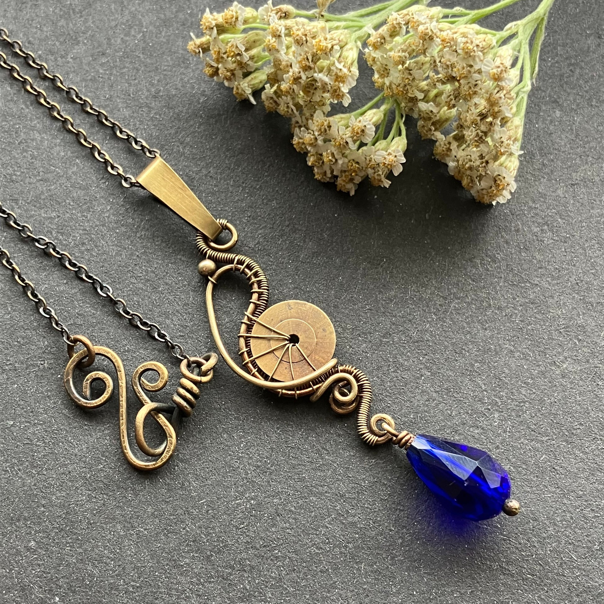 A brass pendant featuring a cogwheel and a deep blue crystal bead