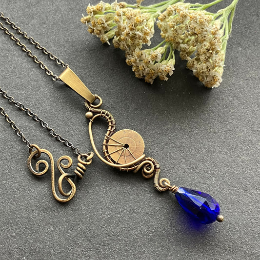 A brass pendant featuring a cogwheel and a deep blue crystal bead